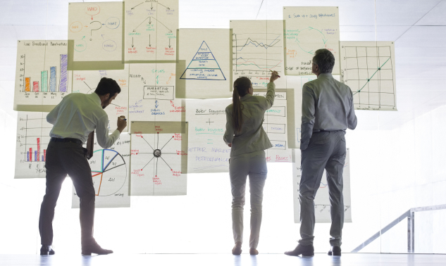 3 people stood in front of a transparent wall covered with data graphs