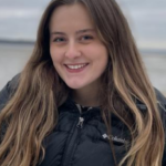 A woman wearing a black jacket on a beach.