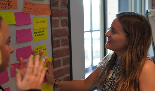 2 women standing next to a wall covered in post it notes