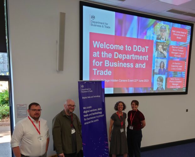 2 women and 2 men stood by a big screen which says 'Welcome to DDaT at the Department for Business and Trade'