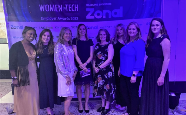 A group of 8 women standing in front of a banner saying Women in Tech