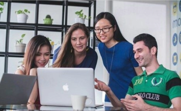 A group of 4 people smiling at a laptop screen.