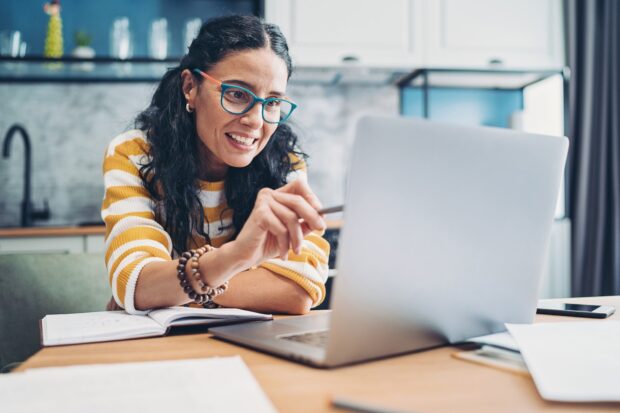 A dark-haired lady with glasses pointing at a laptop with her pen.