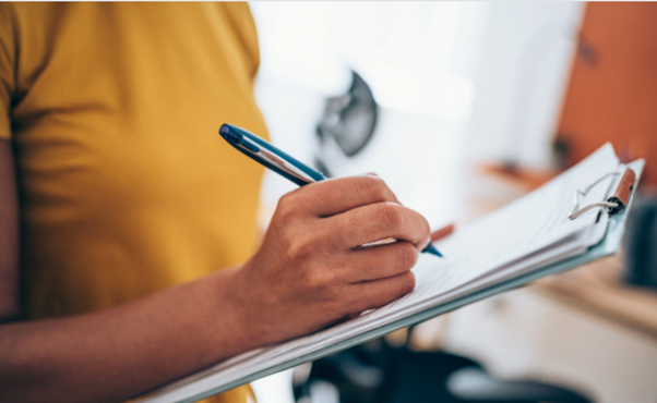 A woman in a yellow top writing on a clip board