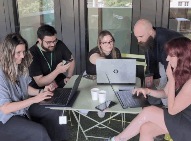 A group of 5 people with laptops gathered around a table.