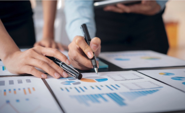 2 people pointing at a print out pie chart with pens.