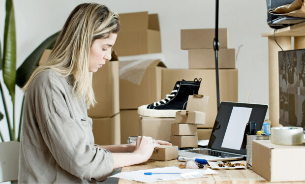 A small business owner packs an order item into a small box on her desk.