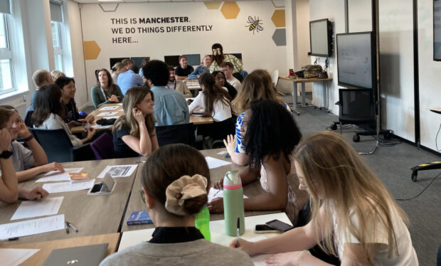 A mixed class of students. 'This is Manchester. We do things differently here' is written on a wall.
